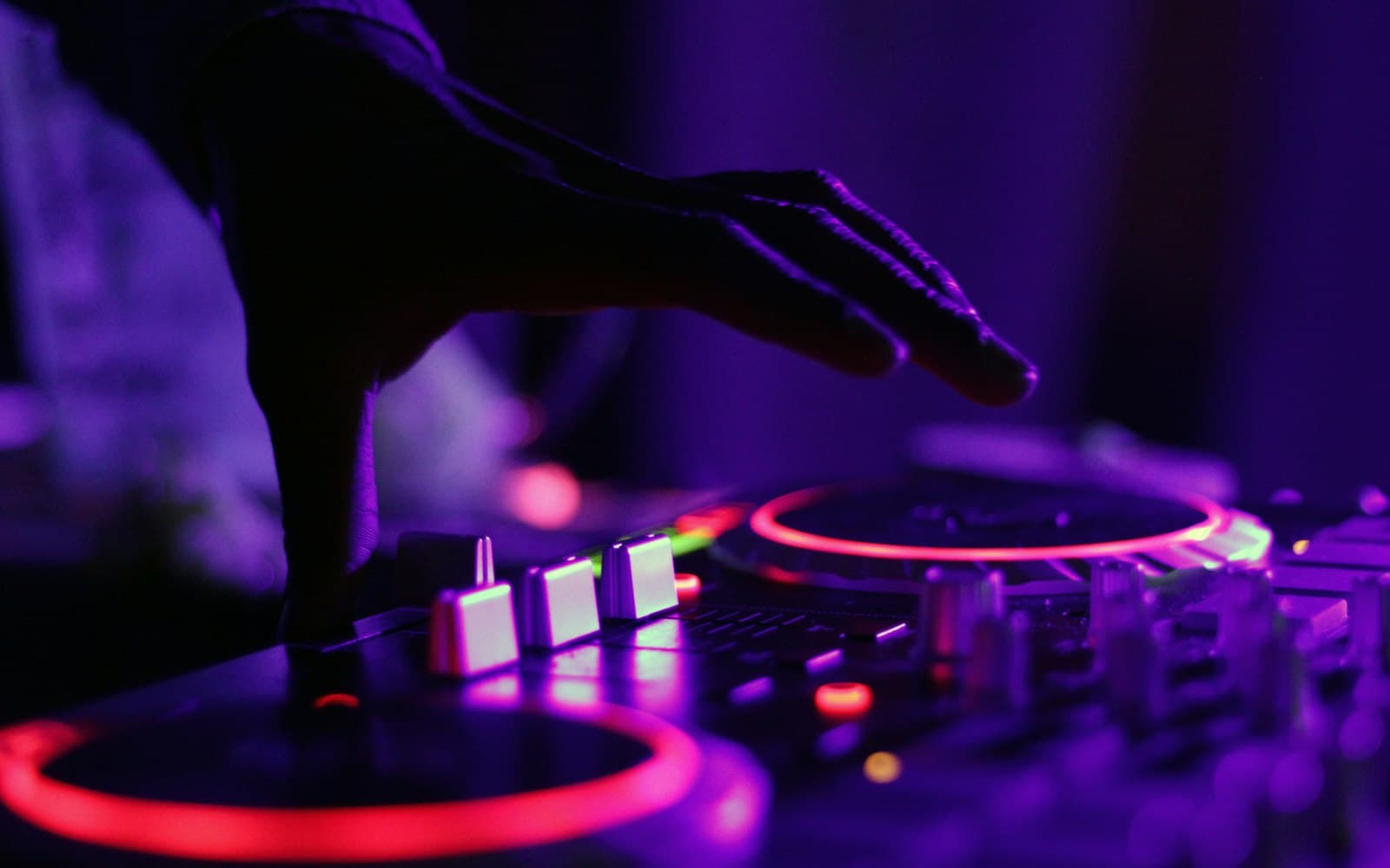 DJ hand poised over a backlit mixing console with turntables glowing red under purple stage lighting