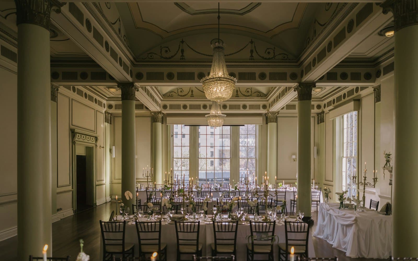 Elegant ballroom with crystal chandeliers, tall columns, and candlelit banquet tables set for a formal seated dinner, a common setting for hotel holiday parties