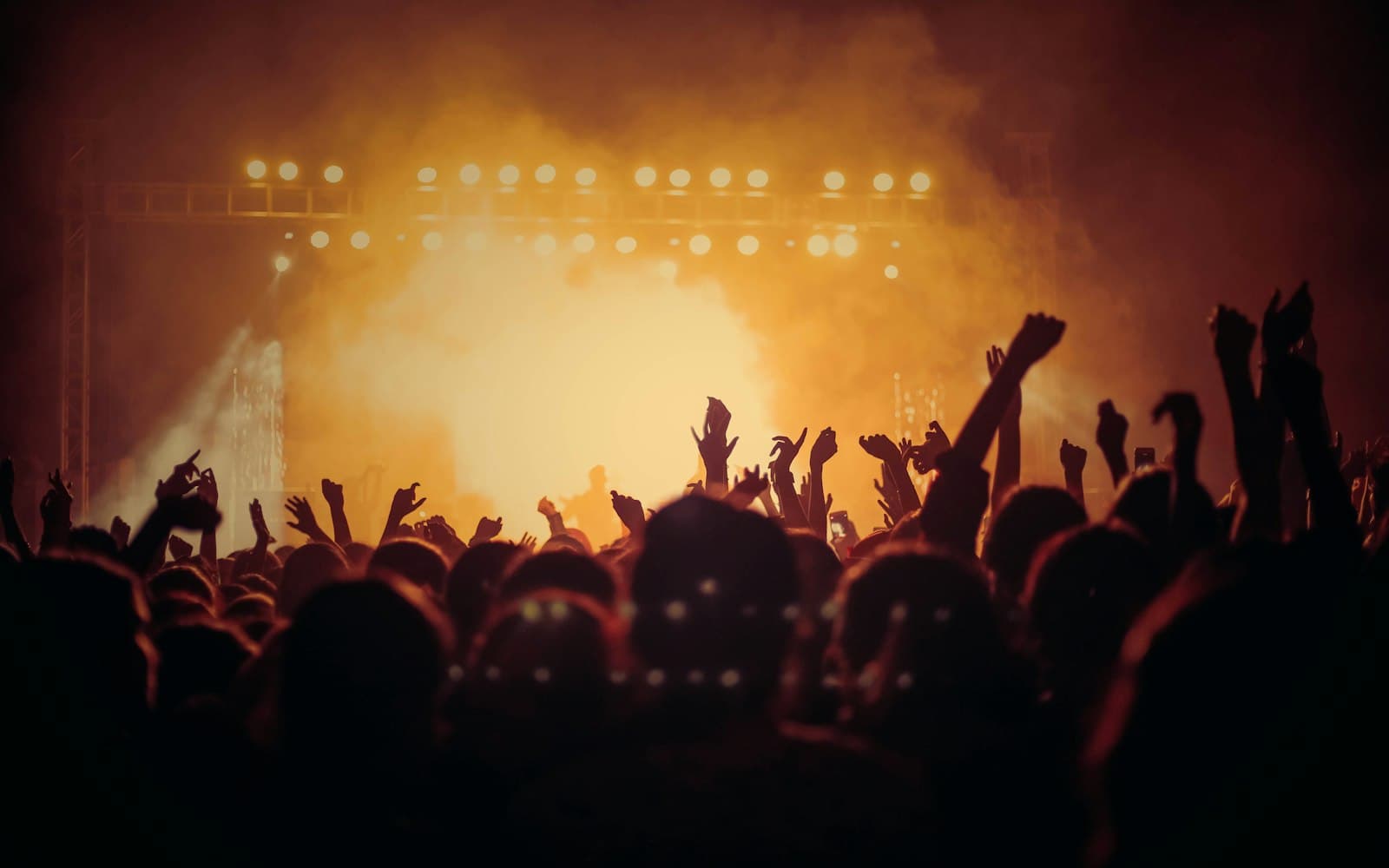 Festival stage truss and lighting bars rigged above an outdoor crowd at dusk