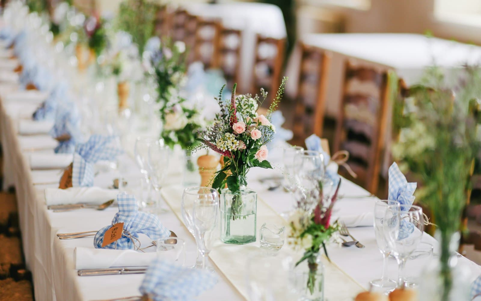 Long wedding reception table styled with white linens, spring florals, and glassware under soft natural light, set for a Tampa Bay wedding dinner