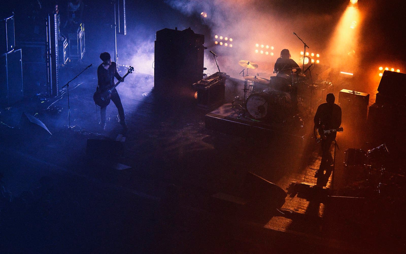 A live band performing on a hazy stage split between cool blue and warm amber light, evoking the choice between a live band or DJ for your event