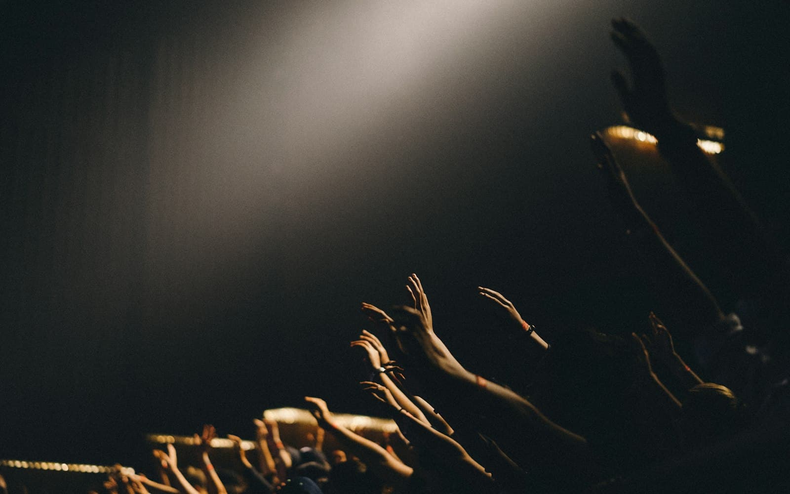 Stage lighting beam illuminating a crowd with raised hands at a live production event, with shadows and atmospheric haze