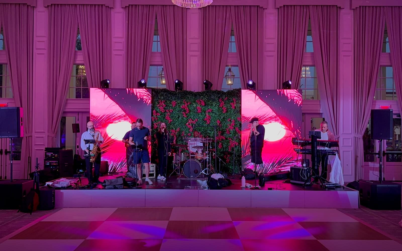 A live band performing on a lit stage at a corporate evening event while professionally dressed guests gather near round dinner tables