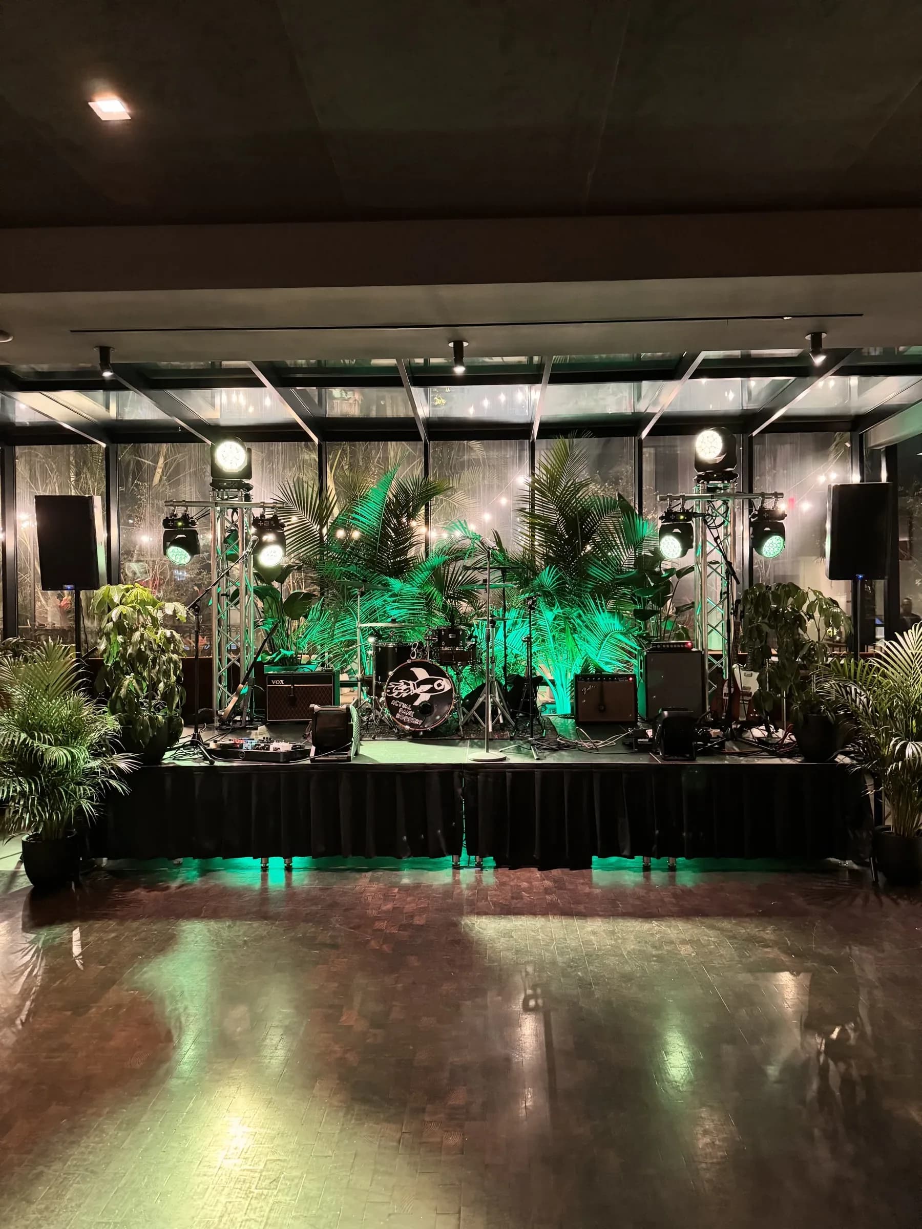 Skirted stage with truss-mounted moving lights, PA speakers, and a full band backline under green uplighting
