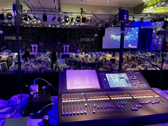 Front-of-house audio console facing a fully-set ballroom under stage lighting at a Tampa event